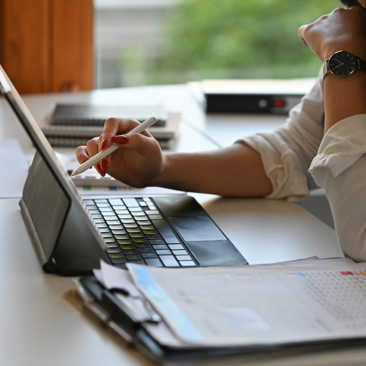 Professional completing licensure paperwork on a tablet with documents and calendar on the desk.