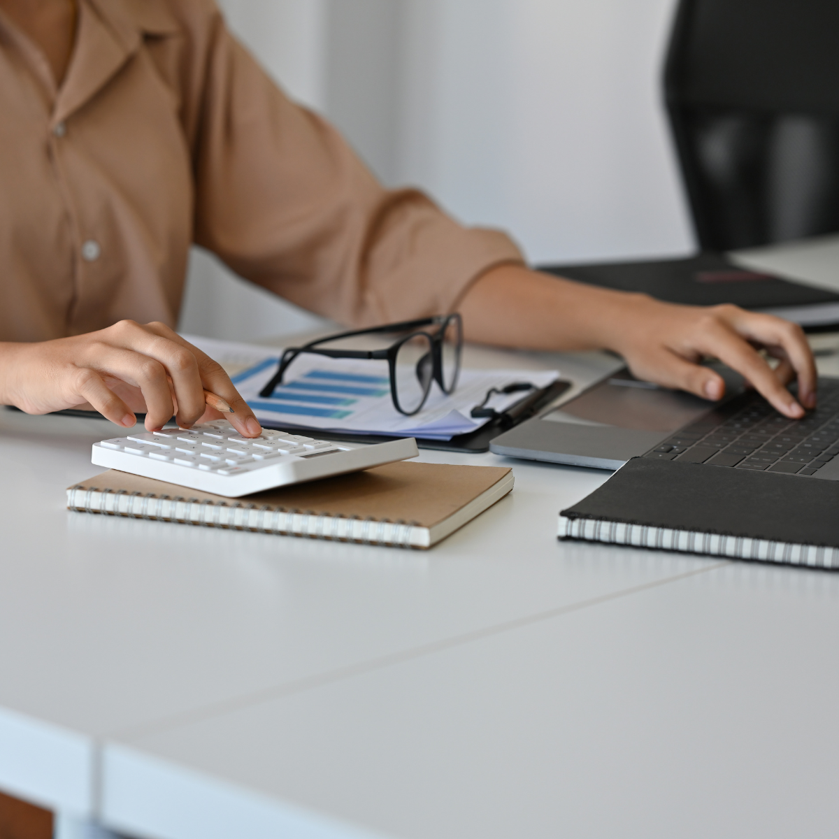 Close-up of a professional managing licensure documents, calculator, and laptop for compliance support.