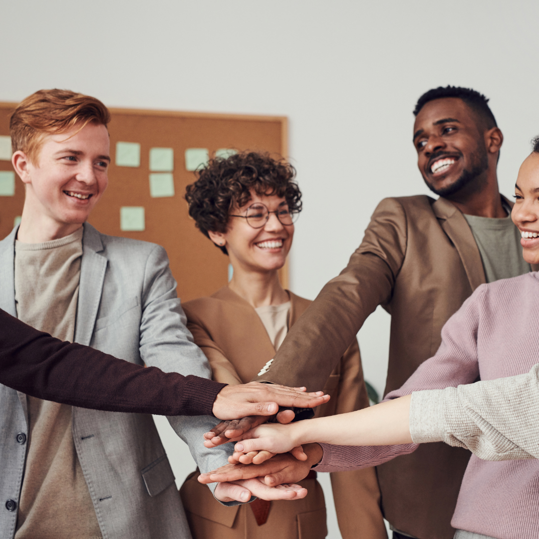 A diverse group of smiling professionals standing in a circle with their hands stacked together in teamwork.