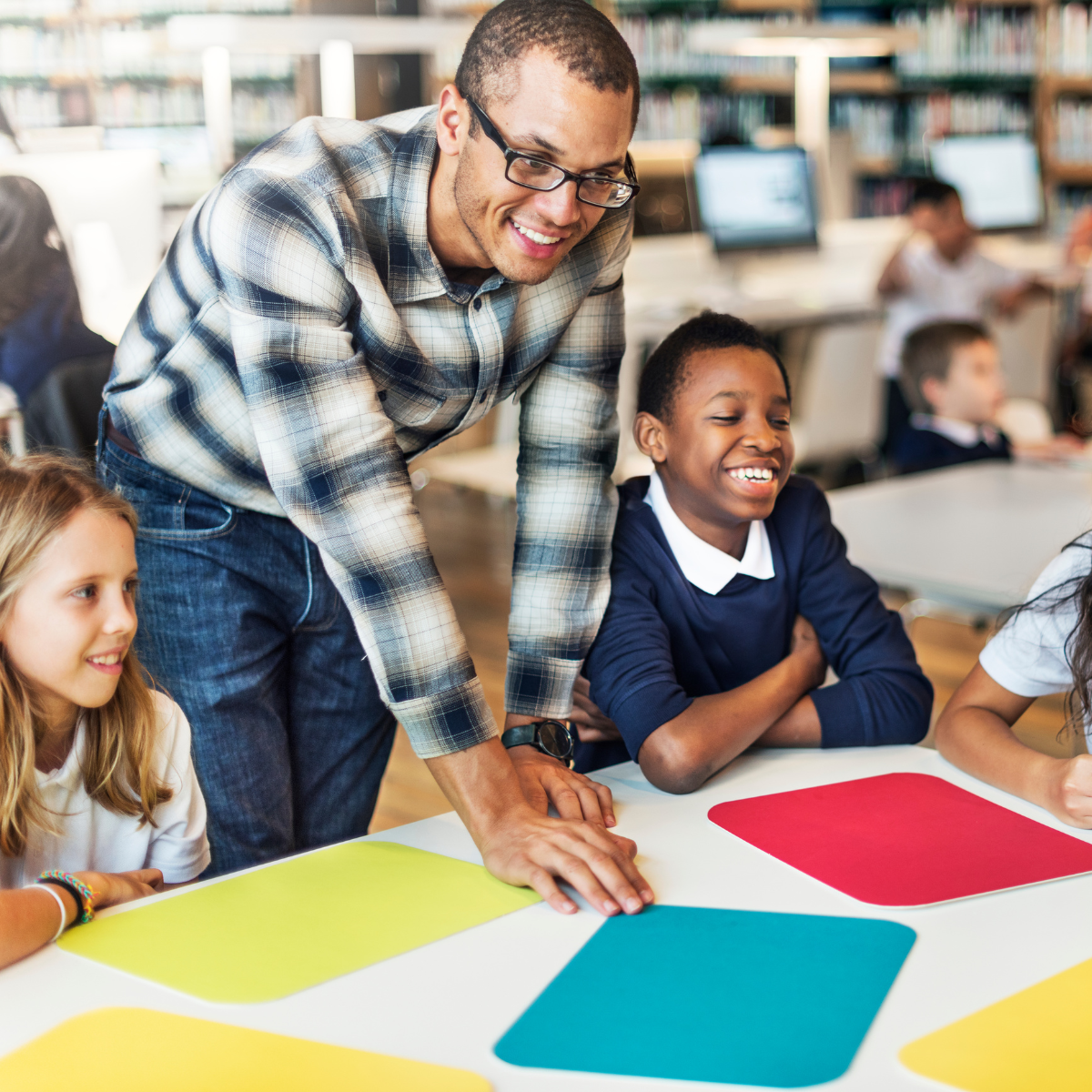 Smiling teacher guiding diverse elementary students during a colorful classroom activity.