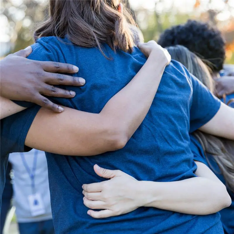 Group of people in blue shirts embracing in a supportive hug at a community event.