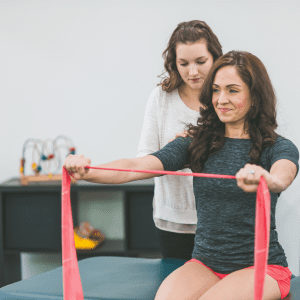 Patient performs a resistance-band exercise during a physical therapy session while a clinician provides guidance. 