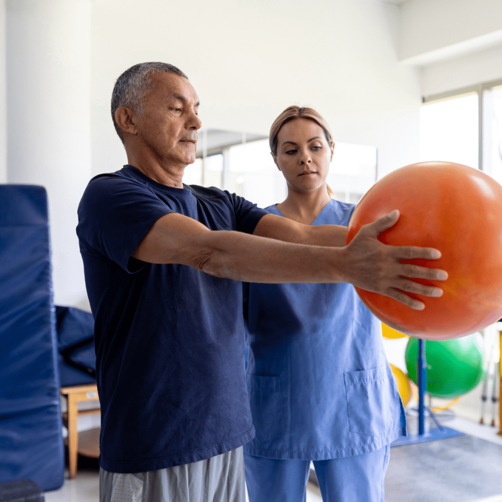 Pioneer PT Pay Insights: Rehab Setting and Patient Care Older patient holds a large therapy ball during a rehab exercise as a clinician supervises and supports proper form.