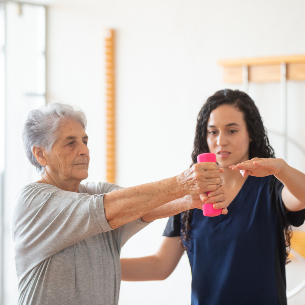 Pioneer Senior Strength Travel Therapy A senior woman working with a Pioneer therapist to improve arm strength using a pink dumbbell.