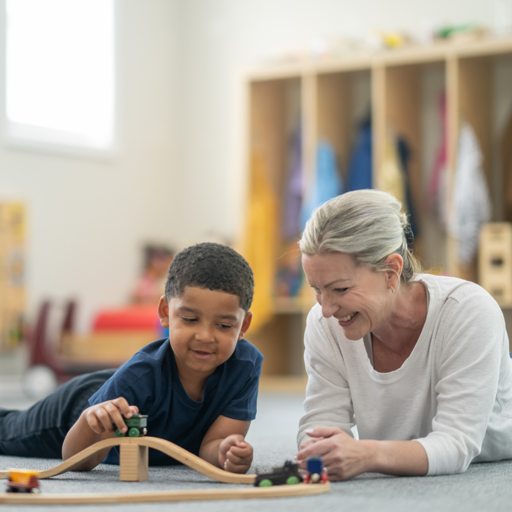 Pioneer Pediatric Play Therapy A young boy and a Pioneer travel therapy specialist playing with a wooden train set on the floor.