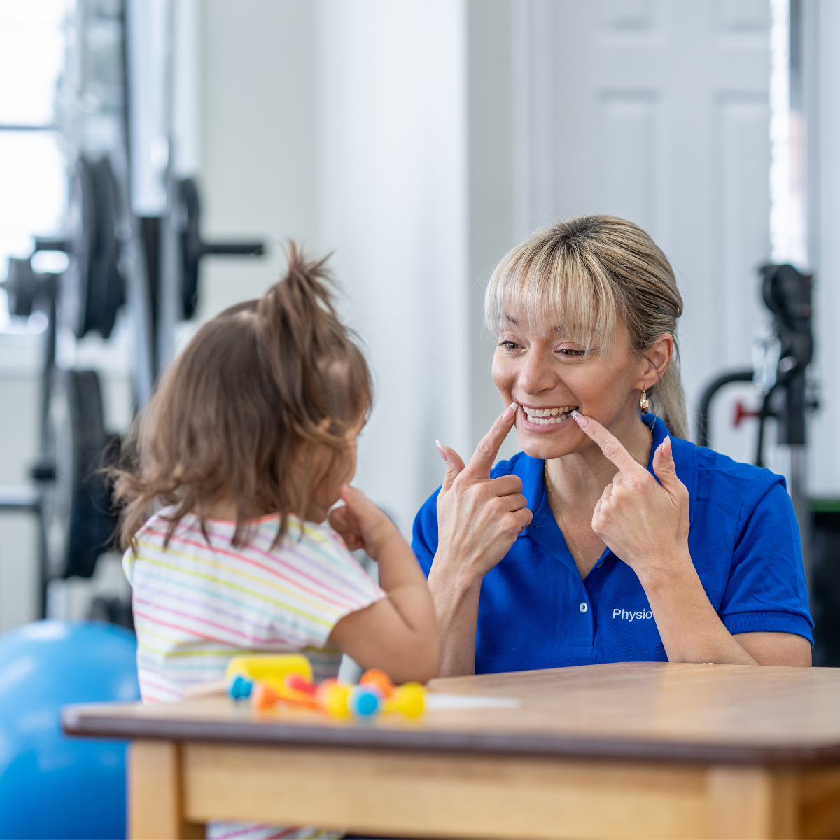 Speech therapy assistant engaging a child in a language development activity using visual cues at a therapy table.