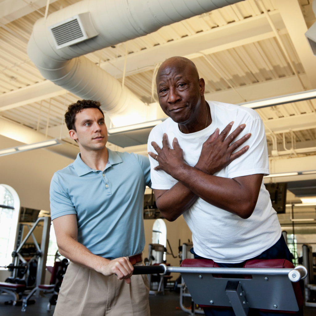 A senior man practicing balance exercises with a Pioneer physical therapy specialist in a gym.