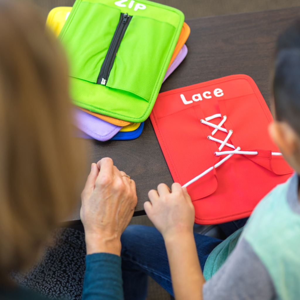 Occupational therapy activity focused on fine-motor skills as a child practices lacing on a learning board with clinician support nearby. 