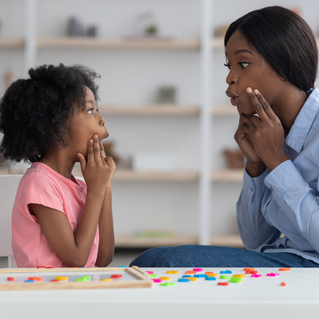 Clinician and child practice mouth and speech movements together during a pediatric speech therapy activity. 