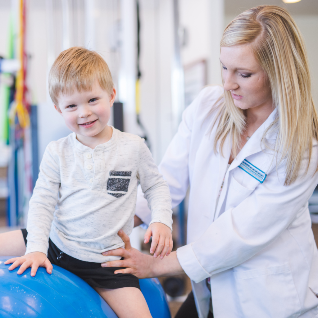 Pediatric physical therapist in white coat helping young child with balance therapy on exercise ball