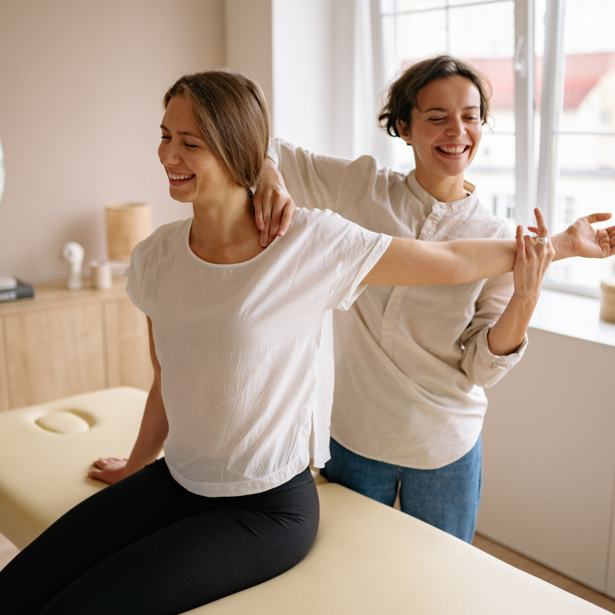 Physical therapist standing behind seated patient helping correct posture and balance during rehabilitation session.
