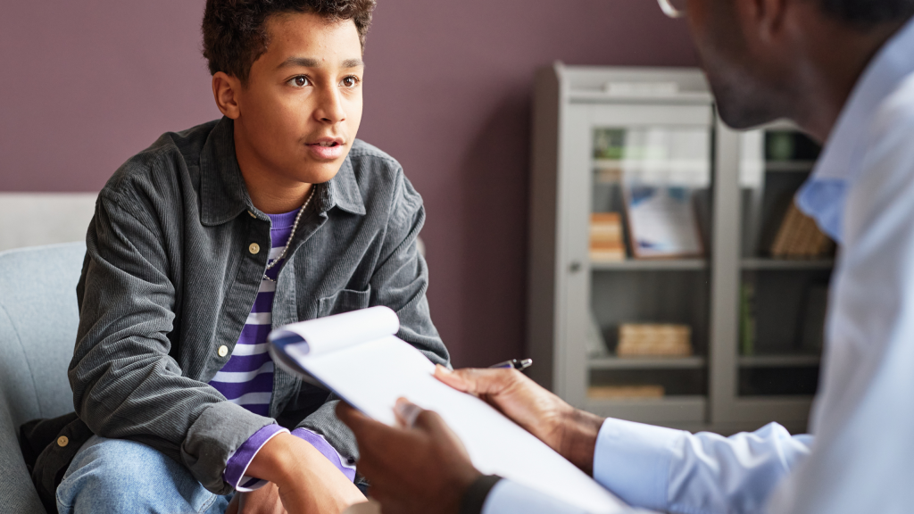 A young man in a therapy session talking to a mental health professional holding a notepad.