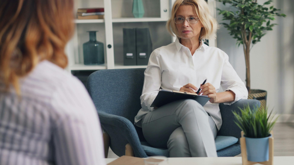 A licensed female psychologist in a striped shirt explaining career path options to a young colleague in a bright office.