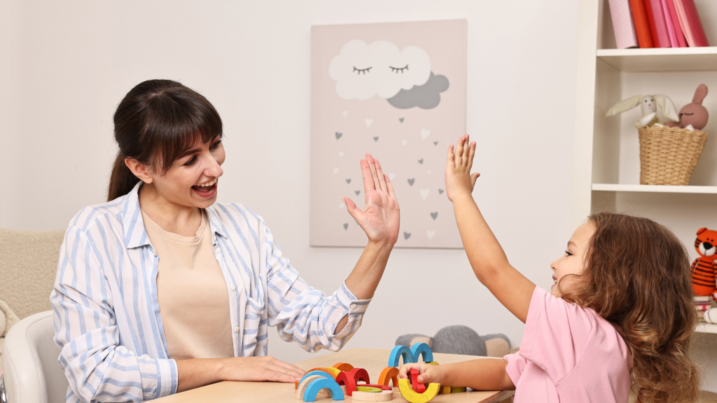 Smiling psychologist giving high five to a little girl at table in a mental health center.
