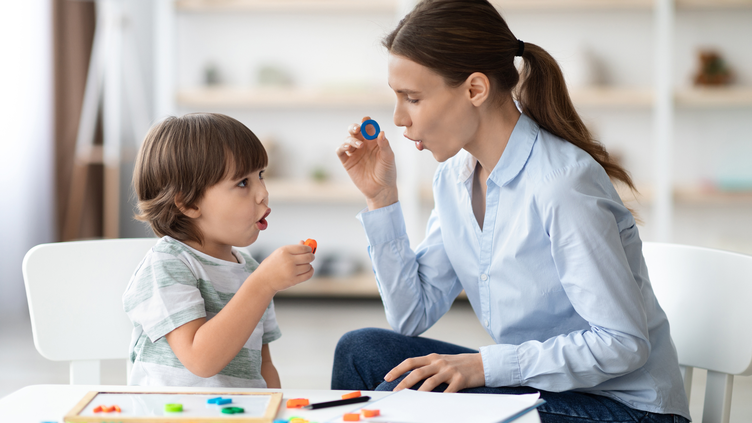 Speech language pathologist working with child on speech sounds using therapy tool during pediatric speech therapy session in clinical setting