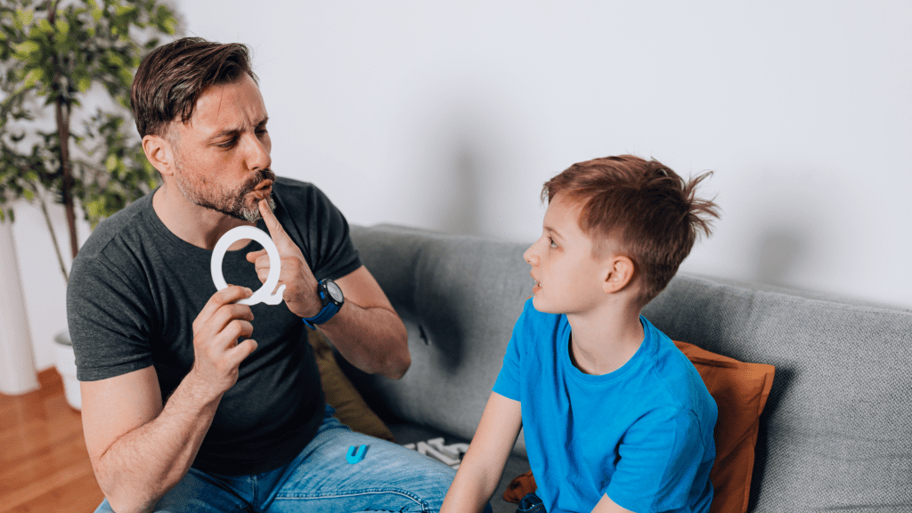 Speech language pathologist guiding child to pronounce sounds using articulation tool during speech therapy session on couch 