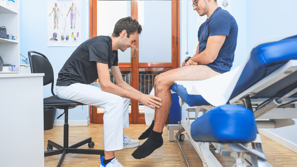 A physical therapist in white pants and a black shirt evaluating a patient's lower leg mobility in a clinical office setting.