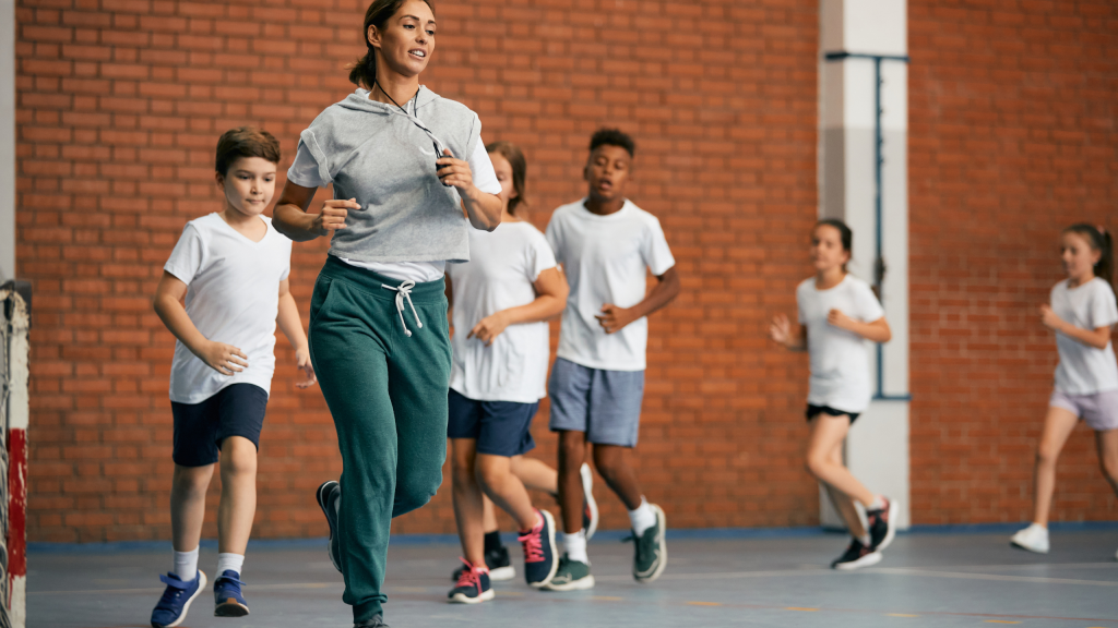 PE Teacher Ideas for Soccer Activities – Engaging Physical Education Curriculum Elementary school coach and group of children running during physical education class at school gym.