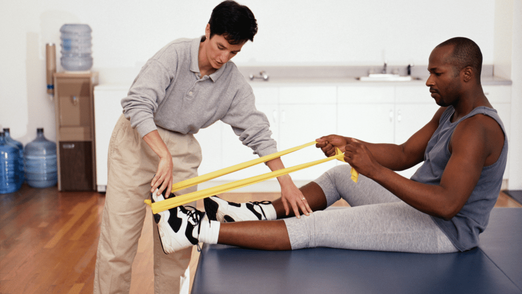 PE Teacher Ideas for Soccer Activities – Engaging Physical Education Curriculum A female physical therapist assisting a male patient with a yellow resistance band leg exercise in a clinic setting.