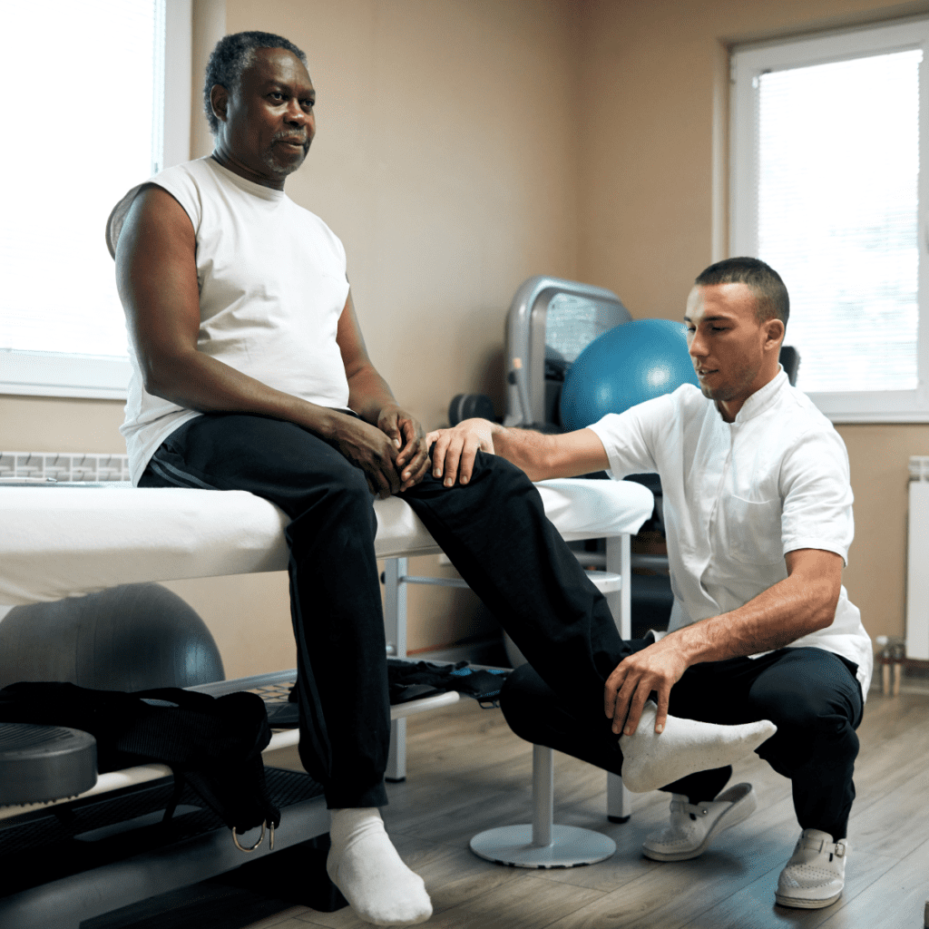 Older patient holds a large therapy ball during a rehab exercise as a clinician supervises and supports proper form.